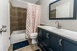 Full bath featuring vanity, shower / bathtub combination with curtain, and dark tile patterned flooring
