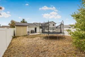 Rear view of house featuring a patio area, a fenced backyard, a trampoline, and a shingled roof