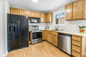 Kitchen with black appliances, light countertops, light wood-style floors, and a textured ceiling