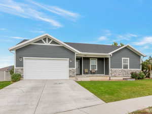 View of front of home with stone siding, concrete driveway, covered porch, and an attached garage