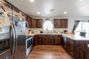 Kitchen featuring appliances with stainless steel finishes, a peninsula, dark brown cabinets, light countertops, and a textured ceiling