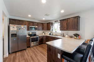 Kitchen featuring dark brown cabinetry, stainless steel appliances, light countertops, a kitchen bar, and light wood finished floors