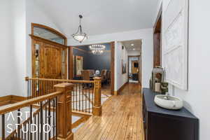 Hallway with light wood-type flooring, a chandelier, and an upstairs landing