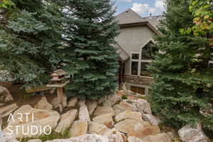 View of side of property featuring a shingled roof, stucco siding, and stone siding