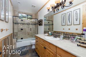 Full bathroom featuring vanity, enclosed tub / shower combo, a wainscoted wall, dark stone finish floors, and backsplash