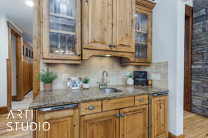 Kitchen featuring glass insert cabinets, dark stone counters, backsplash, and brown cabinets