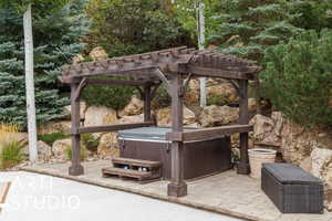 View of patio with a hot tub, a pergola, and view of scattered trees
