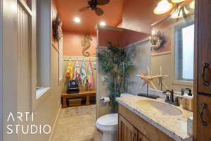 Half bathroom featuring vanity, ceiling fan, light tile patterned floors, and wainscoting