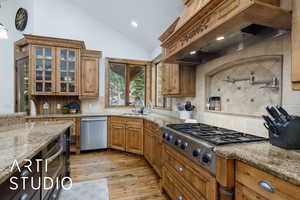 Kitchen with premium range hood, light stone countertops, backsplash, glass insert cabinets, and vaulted ceiling