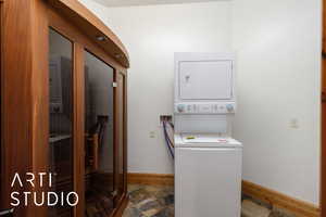 Washroom featuring a sauna / steam room, estacked washer and dryer, and dark stone finish floors