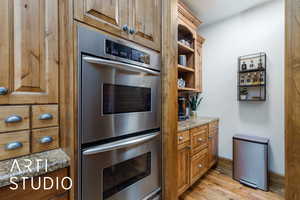 Kitchen featuring double oven, brown cabinets, light wood finished floors, open shelves, and light stone countertops