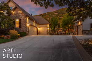 View of front of property with stone siding, an attached garage, driveway, stucco siding, and roof with shingles