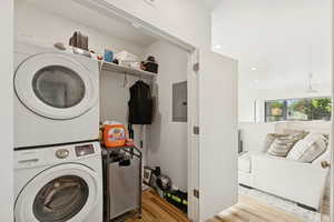Washroom with light wood-style floors, stacked washing machine and dryer, electric panel, and recessed lighting