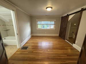 Unfurnished bedroom with light wood-style floors, a barn door, crown molding, and ensuite bathroom