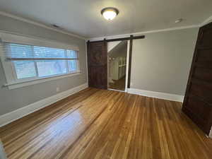Unfurnished bedroom with crown molding, hardwood / wood-style floors, and a barn door