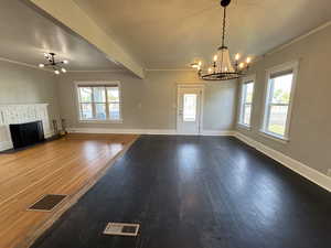 Unfurnished living room with a chandelier, crown molding, dark wood finished floors, and a brick fireplace