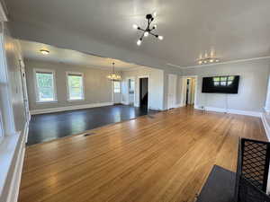 Unfurnished living room featuring wood finished floors, a chandelier, and crown molding