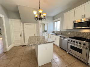 Kitchen featuring stainless steel appliances, pendant lighting, white cabinetry, light stone countertops, and light tile patterned flooring