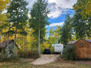 View of side, featuring a gambrel roof, a metal roof, a shed, a standing seam roof, and view of wooded area