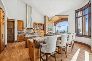 Kitchen featuring brown cabinets, light stone countertops, high vaulted ceiling, glass insert cabinets, and light wood-type flooring