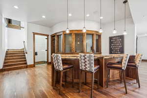 Indoor dry bar featuring light stone countertops, recessed lighting, light wood finished floors, stairway, and hanging light fixtures