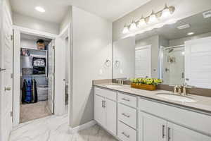 Full bath featuring a shower stall, double vanity, a walk in closet, light marble finish flooring, and recessed lighting