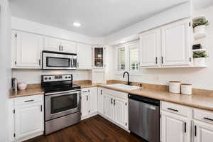 Kitchen featuring appliances with stainless steel finishes, white cabinetry, light countertops, dark wood-style floors, and recessed lighting
