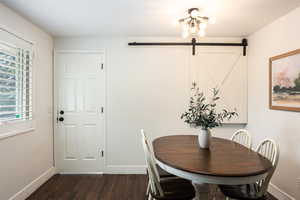 Dining area featuring a barn door, dark wood-style floors, and a chandelier