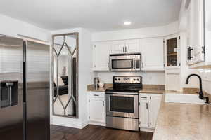Kitchen with stainless steel appliances, white cabinetry, light countertops, dark wood-type flooring, and recessed lighting
