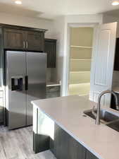Kitchen featuring stainless steel fridge, recessed lighting, dark brown cabinets, light stone counters, and light wood finished floors