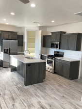 Kitchen featuring a textured ceiling, stainless steel appliances, a center island with sink, light wood-style flooring, and recessed lighting