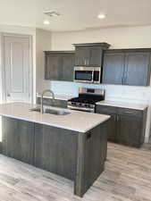 Kitchen featuring appliances with stainless steel finishes, a kitchen island with sink, light wood finished floors, light stone counters, and recessed lighting