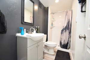 Full bath with vanity, a stall shower, a textured wall, and light wood-type flooring