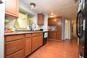 Kitchen featuring black appliances, brown cabinetry, light wood finished floors, and light countertops