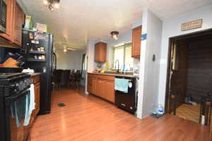 Kitchen featuring black appliances, light wood-style floors, brown cabinetry, and light countertops