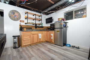 Kitchen featuring open shelves, freestanding refrigerator, light wood finished floors, and dark stone counters
