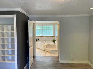 Corridor featuring a textured ceiling, ornamental molding, and wood finished floors