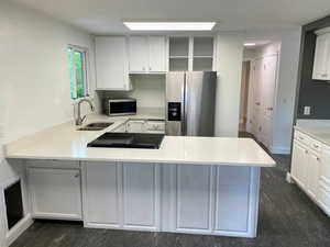 Kitchen featuring stainless steel appliances, white cabinetry, light stone counters, a peninsula, and open shelves