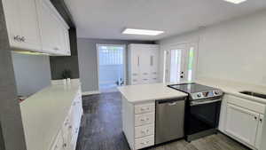 Kitchen featuring white cabinetry, stainless steel appliances, a peninsula, a textured ceiling, and dark wood finished floors