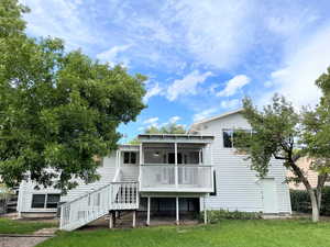 Rear view of house featuring a wooden deck, stairs, and a lawn