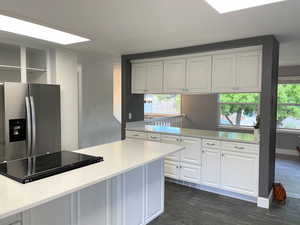 Kitchen with stainless steel refrigerator with ice dispenser, white cabinets, dark wood-style flooring, and light stone countertops