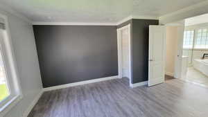 Unfurnished bedroom with crown molding, a textured ceiling, and light wood-style floors