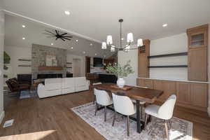 Dining room with a fireplace, wood finished floors, a ceiling fan, a chandelier, and recessed lighting