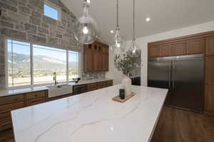 Kitchen featuring stainless steel appliances, vaulted ceiling, brown cabinetry, a mountain view, and light stone counters