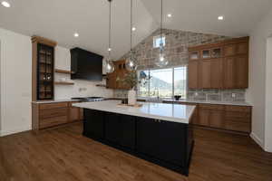 Kitchen with glass insert cabinets, tasteful backsplash, pendant lighting, brown cabinetry, and high vaulted ceiling