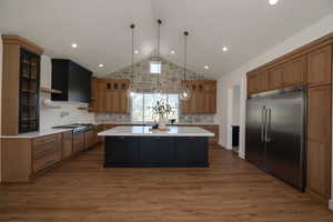 Kitchen featuring stainless steel appliances, tasteful backsplash, pendant lighting, a kitchen island, and high vaulted ceiling