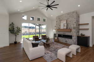 Living room featuring high vaulted ceiling, a stone fireplace, dark wood-style floors, a ceiling fan, and recessed lighting
