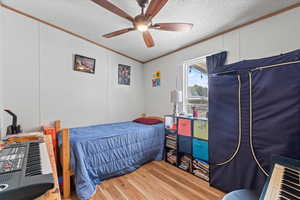 Third bedroom with crown molding, light wood finished floors, a textured ceiling, and ceiling fan