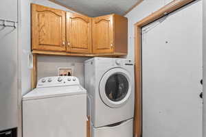 Laundry area with a textured ceiling, separate washer and dryer, and cabinet space