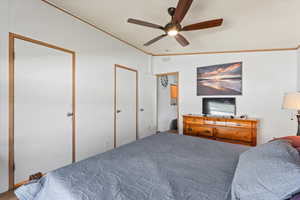 Primary bedroom featuring ornamental molding, a ceiling fan, vaulted ceiling, and two closets